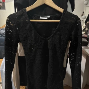 Svart spets topp från Kappahl - Elegant svart spets topp från Kappahl med v-ringning och långa ärmar. Perfekt för en stilren look. Perfekt för sommaren 