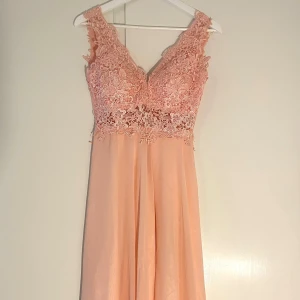 Rosa balklänning med spetsdetaljer - Säljer min fina rosa balklänning med vackra spetsdetaljer på överdelen. Klänningen har en ärmlös design och en flytande kjol som ger en elegant känsla. Jag är 168 cm och den sitter bra i längden på mig 💖💖