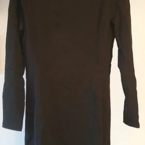 Svart body con-klänning  - Svart klänning i lite tjockare material, detaljer på framsidan av klänningen i form av två parallella linjer som ger en formillusion. 
