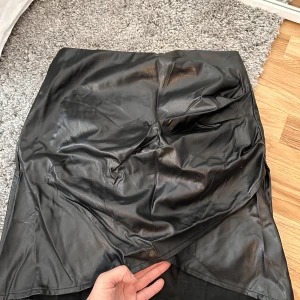 Snygg kjol i skinnimitation - Har en snygg detalj fram i form av att den går upp lite, hoppas ni förstår vad jag menar med bilden. Mer info på sista bilden. Jag är 172cm. Är helt oanvänd! KOLLA GÄRNA IN MINA ANDRA ANONSER, DET MESTA ÄR HELT OANVÄNT 🥰