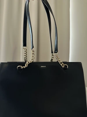 DKNY väska - En DKNY väska som idag är svår att få tag på och som stått och dammat i garderoben.   Väskan är aldrig använd och är pga. Detta i helt nytt skick.   Kvitto samt dustbag finns och medföljer vid köp.