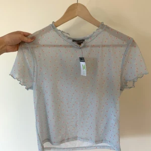 Blommig mesh-topp - Helt ny mesh-topp med etiketten kvar. Står att den ska vara i storlek 40/42 men skulle nog säga att det är en 38/40. Väldigt stretchigt material.