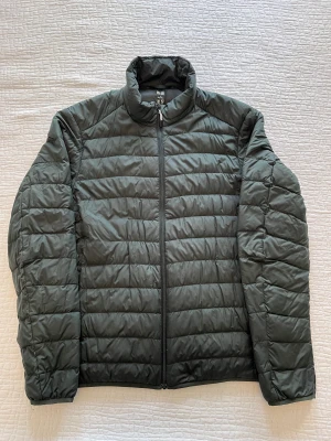 Uniqlo jacka (dunjacka) - En mörkgrön jacka från uniqlo i deras populära modell. Har en tråd som lossnat och dragkedjan är fixad en gång, annars inga fel, se bild 2.