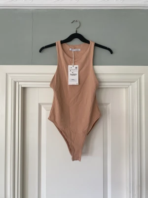 Oanvänd bodysuit - Stretchig, oanvänd, beige/persikofärgad body från Zara. Nypris 150 kr.