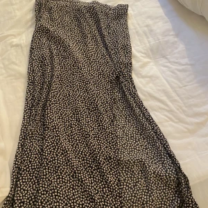 Kjol med slits - Svart kjol med vita blommor, halvlång och slits. Sista bilden är för att visa modellen, de är samma kjol men annan färg! Knappt använd. Strl 40/M