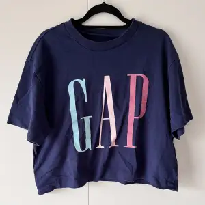 Marinblå croppad t-shirt från GAP i nyskick. Endast använd 2 gånger. Passformen är lite oversize och tyget är något tjockare än vanligt t-shirttyg.