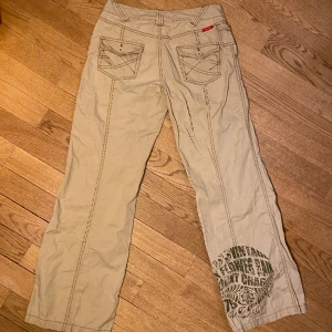 Cargos  - Beigea lågmidjade cargos med tryck på baksidan och jättefina stygn detaljer på bakfickorna.  Storlek 34  Pris kan diskuteras:)