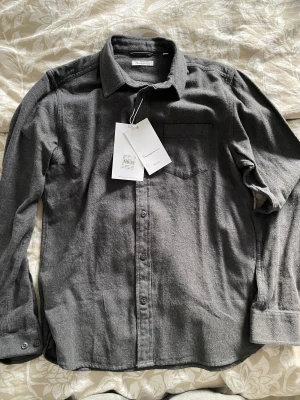 Oanvänd skjorta från Knowledge cotton Apparel - Oanvänd skjorta från Knowledge cotton Apparel med prislapp kvar i storlek S.   Säljes pga av den är för liten för mig. Fått i present.  Skriv om ni vill ha fler bilder.  Material: 100% cotton Nypris 1199 SEK