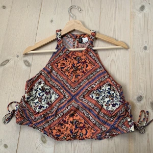 Halterneck Blus - Croppad halterneck blus med knytning på sidorna så man kan justera så den blir kortare/längre. En knapp i nacken.