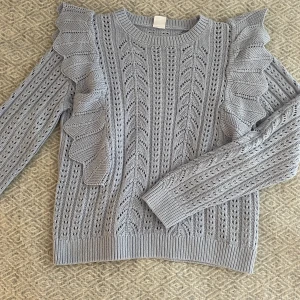 Stickad tröja  - Jätte fin stickad tröja i lila nyans. Den har hål och mönster med två volanger vid ärmarna. Fint skick bara andvänd några fåtal gånger