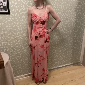 Rosa långklänning - Aldrif använd. Blommigt mönster. Knäppning framtill. Kort underklänning.