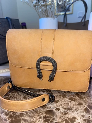 Brun väska  - Brun handväska från Ginatricot.  Använd med lite märken, kan gå att tvätta bort men kan ej lova något.   Gråa kedjor till axelremmar.  Färgen är typ orange brun i färgen. 