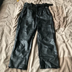 Skinnbyxor  - Highwaisted Kostymbyxor i fuskskinn med skärp. Innerbenslängd 66 cm.