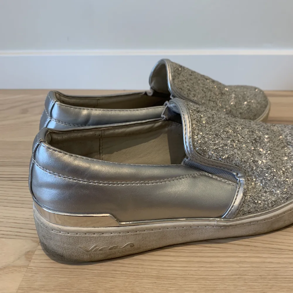 Glittriga silver slip-on skor i storlek 38. Bra skick. Använt de några enstaka gånger. Innersula i läder. . Skor.
