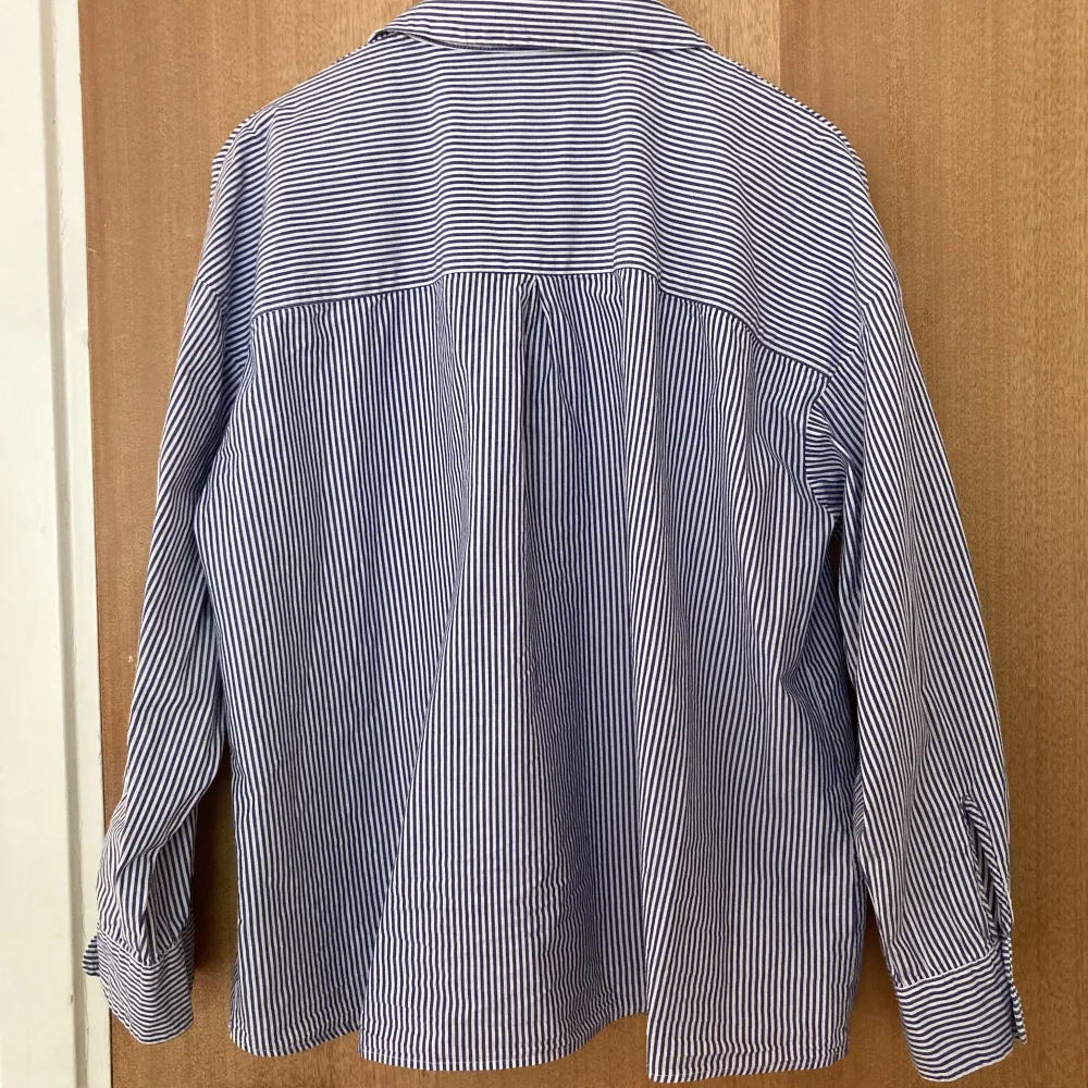 En blå- och vitrandig bomullsskjorta, sitter löst och går ungefär till höften. Den är sval och perfekt för sommaren, i fint skick:) Skriv för närmare bilder/mått m.m.. Skjortor.