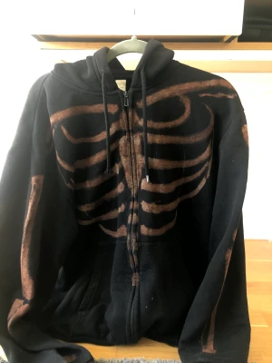 Svart zip up - En svart zip-up hoodie med ett tryck av blekningsmedel