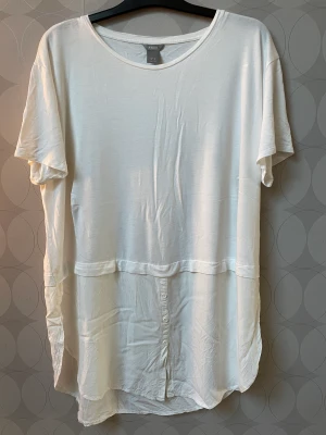 Helt ny lång blus/tunika  - Helt ny (endast testad) vit längre blus/tunika från Lindex i storlek XL, normal till rymlig i storleken.  Kortärmad och med fina, enkla och stilrena detaljer. 