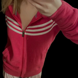 Rosa adidas jacka med mjukt material och i bra skick  - Den här jackan är i perfekt skick utan några fel, den har luva och den är lagom varm och den säljs bara för att jag behöver rensa ut garderoben, bara generellt bra, även lapparna på insidan är kvar och kedjan funkar som den ska.