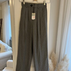 Randiga kostymbyxor  - Ett par mörkgråa kostymbyxor med ljusa ränder i. Aldrig använda, prislappen kvar. 