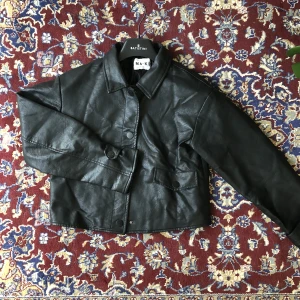 Kort skinnjacka - Riktigt snygg skinnjacka i fake läder. Oversized stil och en aning croppad så slutar lite över midjan.  Inget slitage och är i bra skick. Köpt på NAKD för några år sedan! Skriv för fler bilder eller frågor.