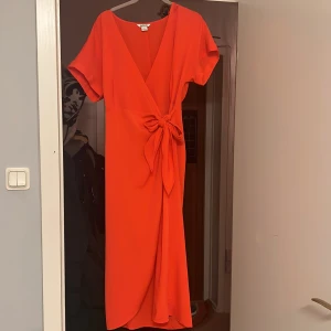 Omlottklänning - Supersnygg rödorange omlottklänning från Monki. Använd en gång. Som ny. Storlek small men beroende på hur man vill att den sitter så passar den även en 38-40.