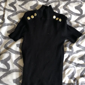 Tröja - En svart tröja med guldiga detaljer i storlek s
