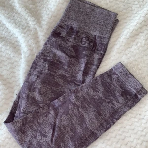 Gymshark tights - Ett par lila camo tights från Gymshark i strl M. Använda men i väldigt bra skick. Scrunch i bak, logga på sidan av höften och längst ner på benet. 
