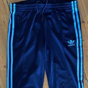 Adidas trackpants i blått och turkost.  Fint skick, förutom en liten fläck nere på ena benet, syns knappt.  Storlek S. Med knytband i midjan, så kan funka till XS också. Raka men lite utsvängda nertill. 