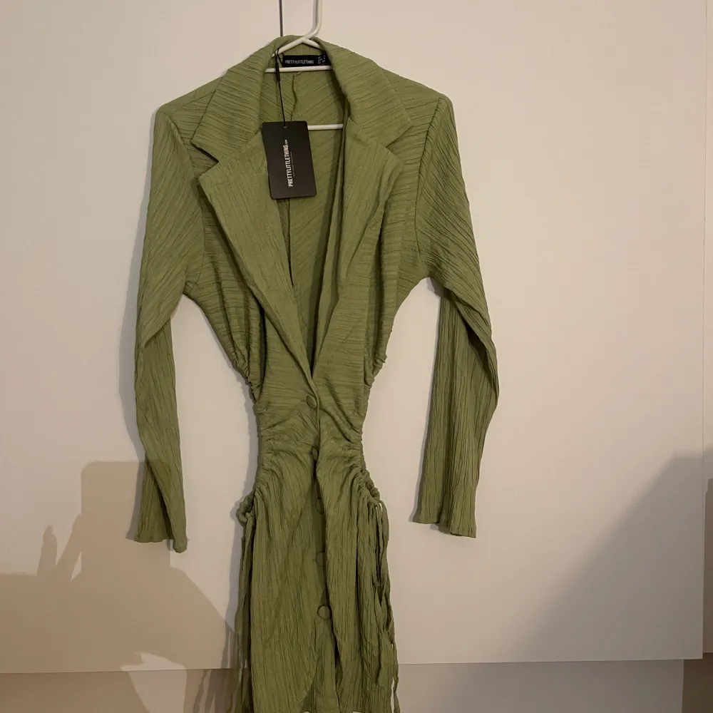 Helt oanvänd grön skjortklänning från Prettylittlething med cut outs på båda sidor som går att justera själv. Det är i storlek 8 (UK size) . Klänningar.