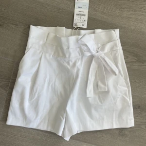 Vita shorts med veck och knytdetalj - HELT NYA! Shorts från Zara med lapp kvar. Högmidjade med veck och knytdetalj. Kommer tyvärr inte till användning hos mig. Nypris 30$.