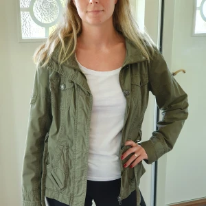 Vår, sommar och höstjacka - En skön jacka från Vila. Huvan är avtagbar. Det saknas en knapp fram, men det är ingenting som märks då man använder dragkedjan. Fint skick i övrigt, knappt använd.  