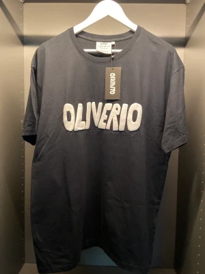 Original OLIVERIO Tee (Osläppt) - Original OLIVERIO Tee från en osläppt klädkollektion. Denna kollektion inkluderar t-shirts samt luv tröjor som är tillgängliga i begränsad upplaga.   - 100% bomull  - 120GSM  - Passform: Oversize  - Färg: Svart / Vit  SKICK: OANVÄND