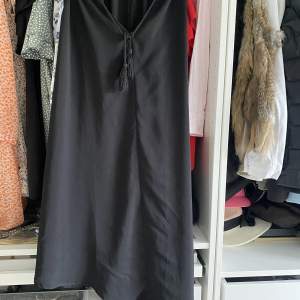 En svart Midi-klänning med lite bohemisk stil. Det följer även med ett band i midjan. Klänningen är snedskuren. Fint skick!