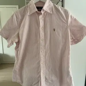 Rosa-vit randig kortärmad skjorta i storlek M från Polo Ralph Lauren. Skjortan har inga fläckar eller tecken på slitage. Säljer pga att jag inte använt skjortan på väldigt länge.