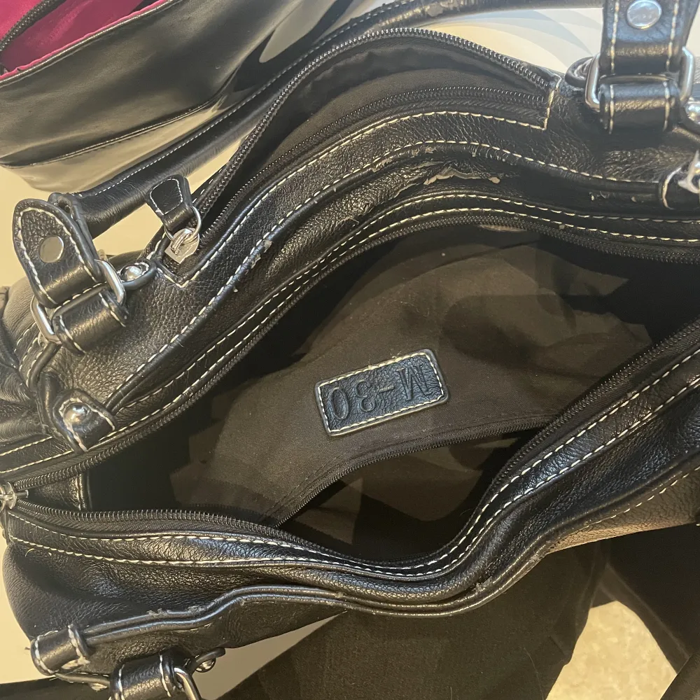 En svart liten/medel handväska i svart ”läder/skinn”. Silvriga detaljer och väldigt rymlig med många fickor inuti. Knappt använd, fint skick. Osäker på märke då den är köpt här på plick.. Accessoarer.