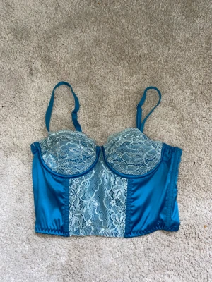 Blå korsett  - Blå klyschig korsett. Skulle säga att kuporna är i storlek A och toppen XS. Använd endast 1 gång och säljer pågrund av förliten. Frakt ingår i priset