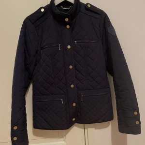 Höst/vårjacka - En lätt frodrad jacka i en marinblå färg och guld detaljer. Den är i bra skick och knappt använd. Storlek 36 och är normal i storleken. Den är köpt på mq och nypris ca 1500kr.