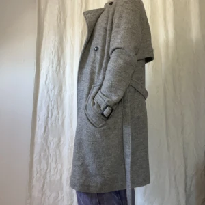 Ullkappa från Samsoe  - Gråmelerad kappa med svarta knappar från Samsoe Samsoe. Slutar strax under knäet på mig (är 173 cm). Fungerar året om med extra tröja/fleece/kofta undertill på vintern. Skärp. 2 fickor + innerficka. Ställbara ”skärp” vid ärmens slut. Ljussgrått innerfoder