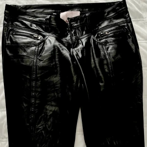 Skinn byxor - Svarta Italienska byxor, skinn imitation, sömmar som går ner längs benens framsida, de är från Baby Angel Fiorucci och designade av Elio Fiorucci. Storlek 42 i italiensk så aningen mindre i EU. Lappen i byxorna sitter inte fast särskilt hårt/hänger i tråd