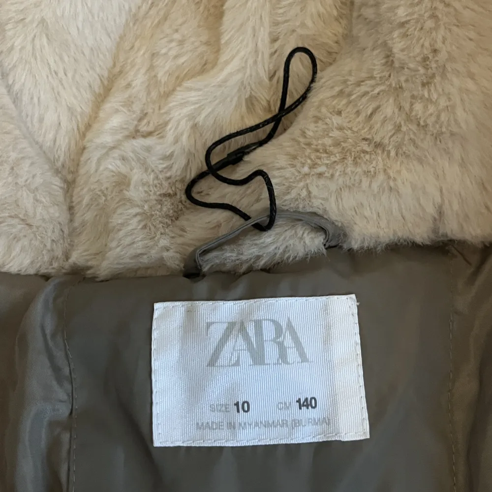 Skön täckjacka från Zara. Supermjukt foder innanför luvan. Modellen är rymlig och går ner en bit över låren. Knappt använd, bara enstaka gånger. Guldiga detaljer och dragsko vid midjan. (Passar mig som är 150 cm lång.). Takit.