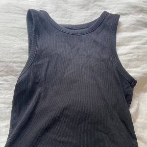 Svart linne - Kortare svart ribbat linne, tjockare över axlarna och öppet vid armarna. 