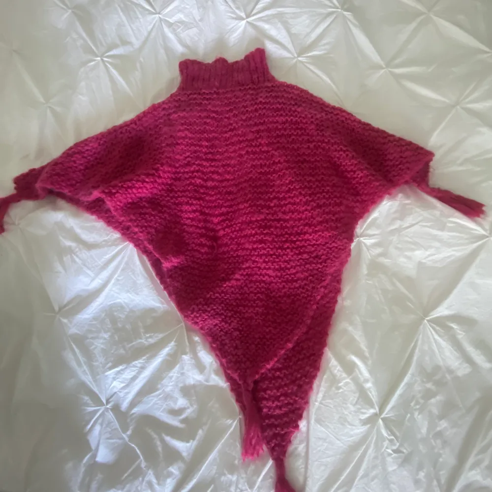 Hemstickad rosa poncho. Snyggt grov stickad med tofsar vid ärmarna, baktill och framtill. Resårstickad halskrage. . Övrigt.