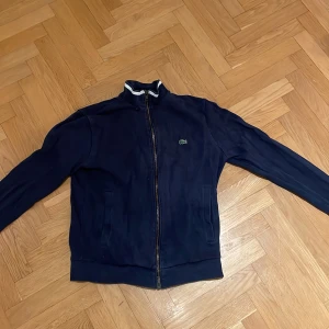 Lacoste tröja - Tröjan är i använt skick och har ett litet hål i första lagret av tyget uppe vid kragen på höger framsida