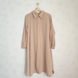 Beige lång skjorta guldknappar - 🥐FÖRST TILL KVARN!🥐 Super classy beige långskjorta med fina guldknappar. Spetsig krage och ger en proffisionell edge till en fin daglig look. Har knappar vid både ärmslut och stängs med både knappar och dragkedja i bak