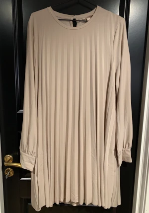 Långärmad plisserad klänning - Beige långärmad plisserad klänning från H&M i storlek L med tillhörande underklänning. Aldrig  använd därför nyskick