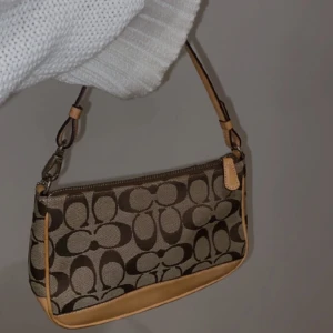 Coach Bag Brown  - ❗️Priset kan diskuteras❗️En lite äldre väska som fortfarande är i bra skick, jag köpte väskan för ca 1200! Det är liten väska med ett kort beige/brunt handtag. Måtten är ca 14x10cm