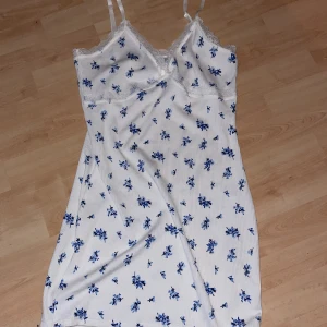 Vit klänning med blåa blommor med vit spets och tunna band - En vit klänning med blåa blommor som är ribbad och bra passform