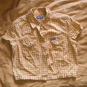 Gul crop top - Kort kortärmad gulrutig skjorta med två bröstfickor. Antagligen 80 lr 90-tal. Storlekslappen säger S, jag skulle säga XS. Passar inte om man har större byst. Jättebra begagnat skick. Material: Bomull.