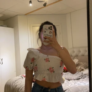 One off shoulder topp - One off shoulder crop top, mönster rosor. Den är stretchig och ej see through. I strl XS-M. Ny skick