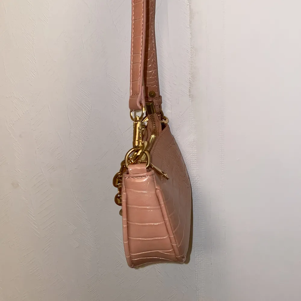 En liten ”gammelrosa” väska med gulddetaljer och krokodilmönster. Väskor.